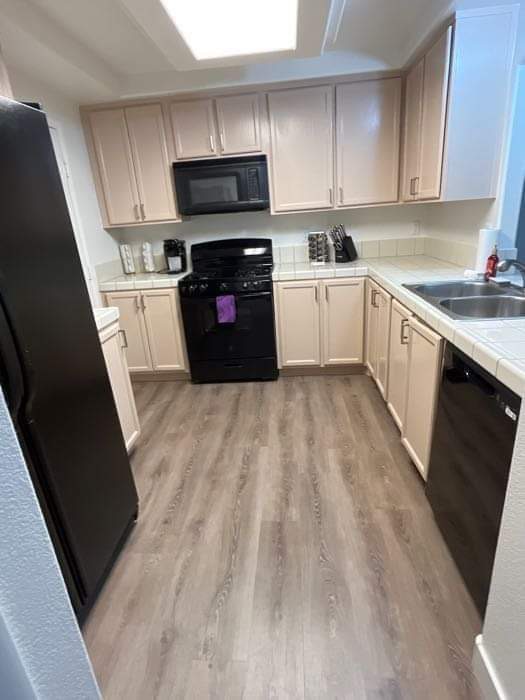 Clean kitchen with light cabinets, black appliances, and wood-look floors